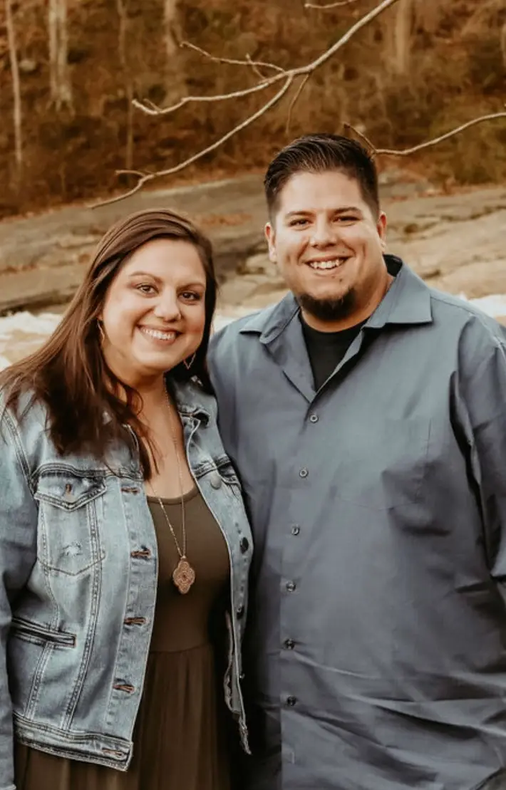 Author Dustin Arrieta standing beside his wife, Laura, outdoors.